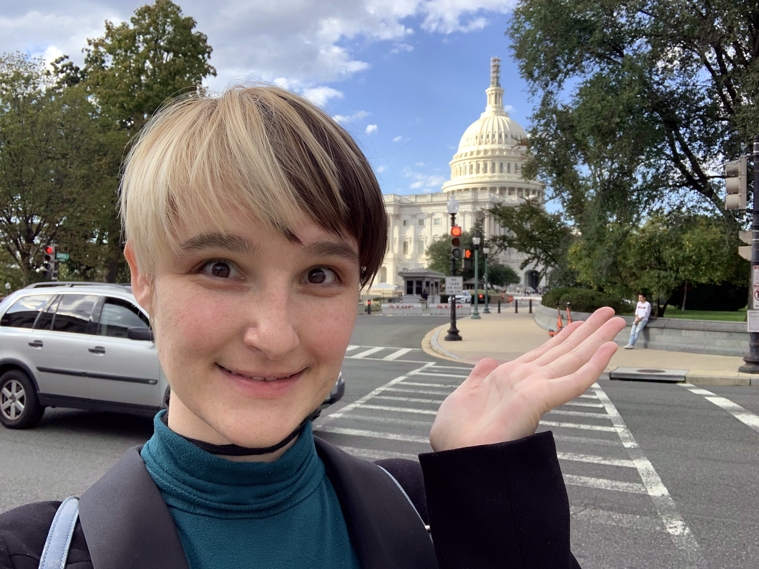 B stands in front of the US Capitol holding up a hand to gesture toward the iconic dome